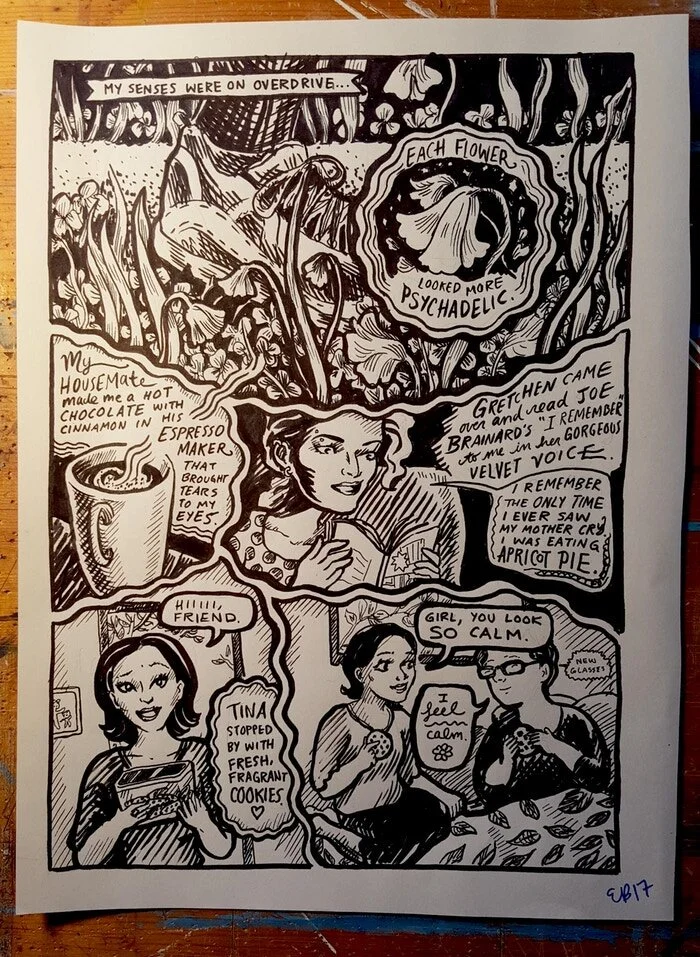 A photograph of an original hand drawn page on a wooden table beside a mug of coffee, the ink lines and hand lettering visible on the paper.